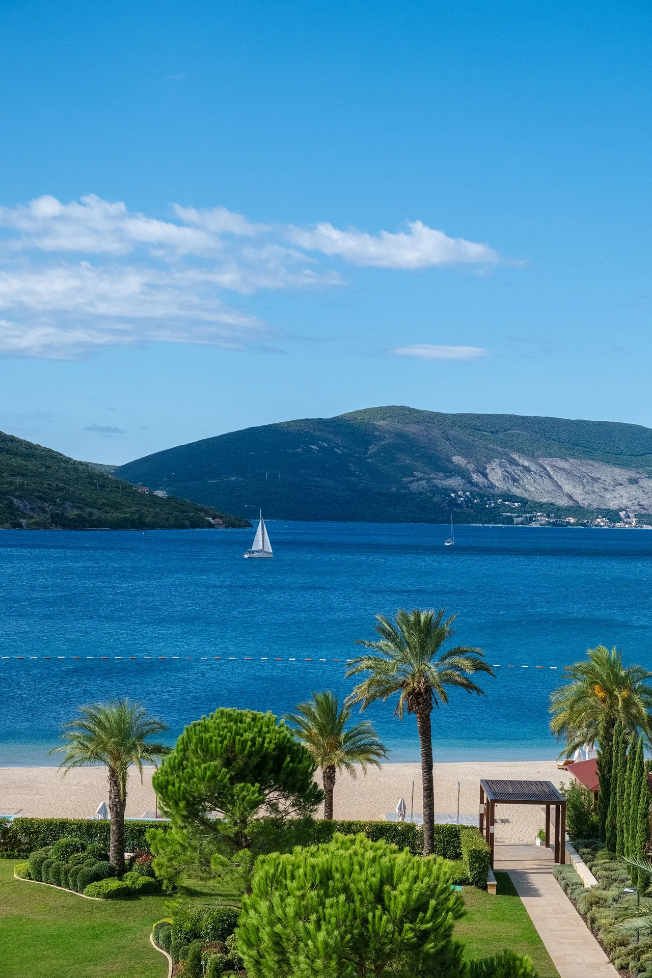 A sailboat on a deep blue bay below green hills