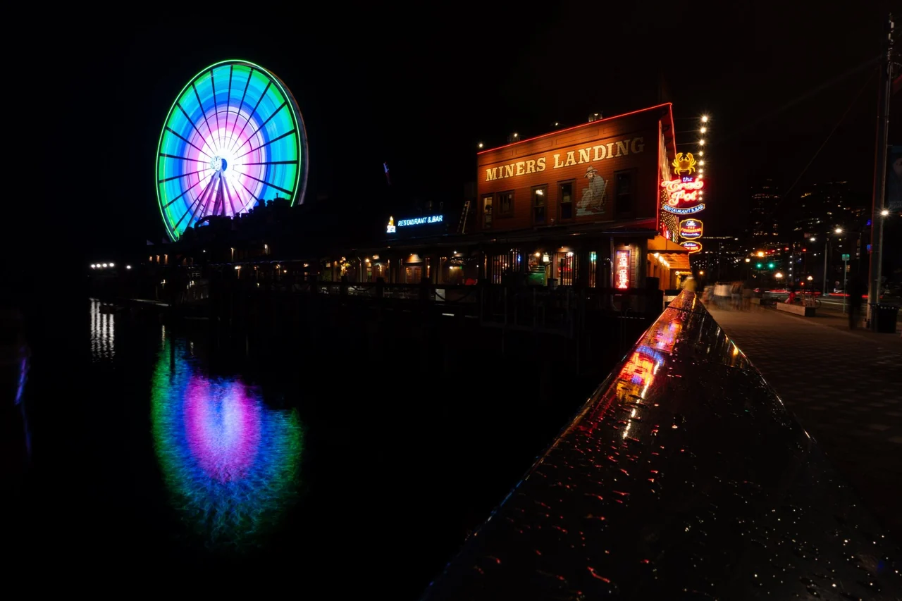 The Great Wheel and Miners Landing lit up at night on the Seattle waterfront
